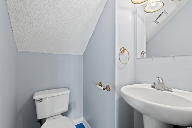 bathroom with toilet, lofted ceiling, a textured ceiling, and sink