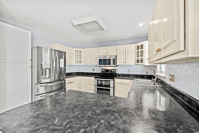 kitchen featuring dark stone countertops, stainless steel appliances, decorative backsplash, and sink