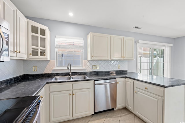 kitchen featuring kitchen peninsula, backsplash, sink, light tile patterned floors, and appliances with stainless steel finishes