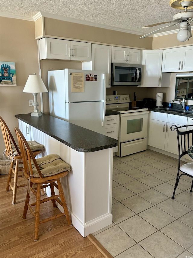 kitchen featuring white appliances, dark countertops, a sink, and white cabinetry