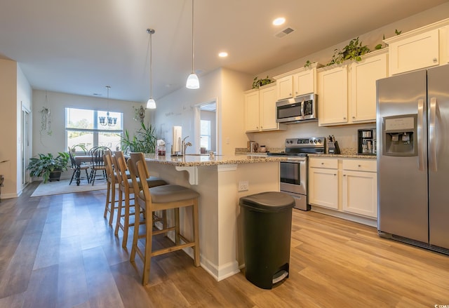 kitchen with appliances with stainless steel finishes, white cabinetry, light hardwood / wood-style floors, decorative light fixtures, and a center island with sink