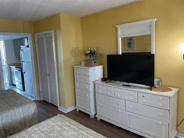 bedroom featuring a closet, a textured ceiling, stainless steel refrigerator, and dark hardwood / wood-style flooring