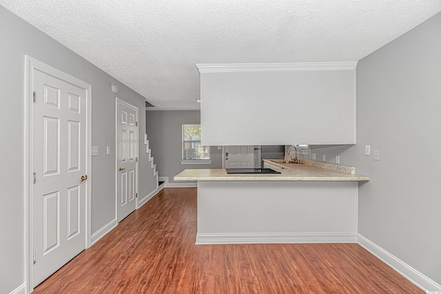 kitchen with wood finished floors, baseboards, a peninsula, light countertops, and a textured ceiling