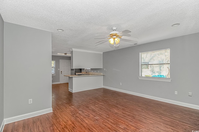 unfurnished living room with dark wood finished floors, plenty of natural light, baseboards, and ceiling fan