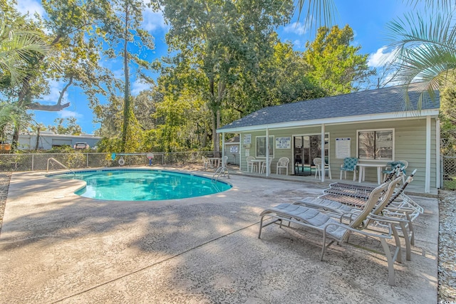 community pool with a patio area, an outbuilding, and fence