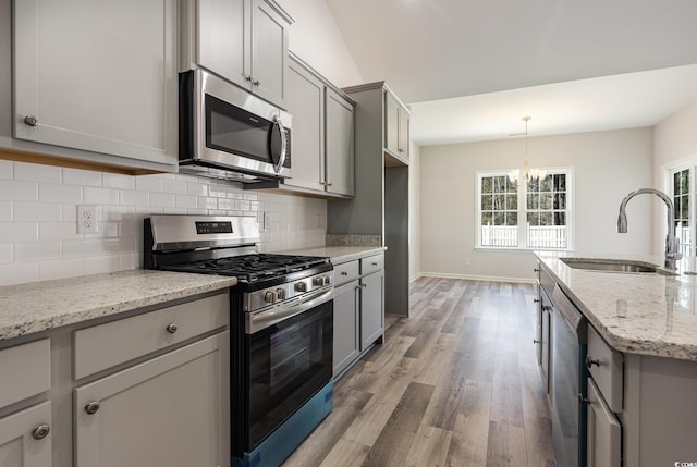 kitchen featuring an inviting chandelier, stainless steel appliances, gray cabinetry, light stone countertops, and sink