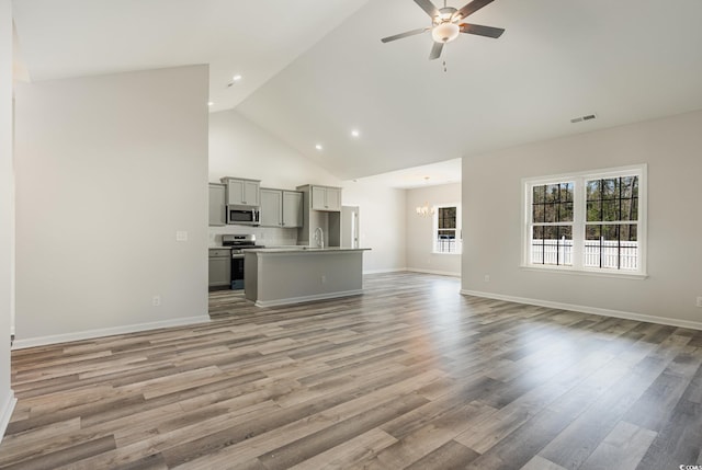 unfurnished living room featuring light hardwood / wood-style floors, sink, high vaulted ceiling, and ceiling fan with notable chandelier