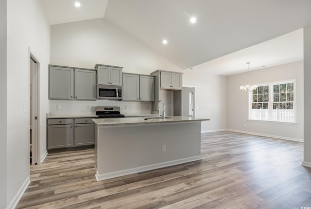 kitchen featuring high vaulted ceiling, gray cabinets, stainless steel appliances, and a center island with sink