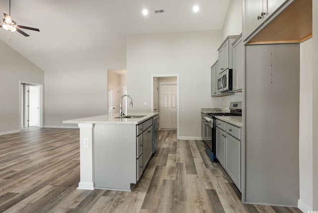 kitchen with gray cabinets, a center island with sink, sink, stainless steel appliances, and high vaulted ceiling