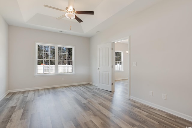 unfurnished room featuring light hardwood / wood-style floors, a tray ceiling, and ceiling fan