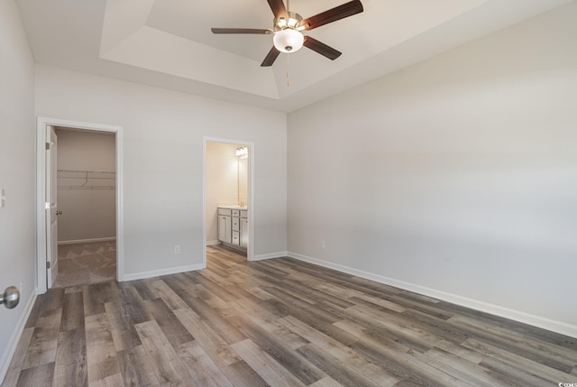 unfurnished bedroom with a spacious closet, ceiling fan, connected bathroom, a tray ceiling, and a closet