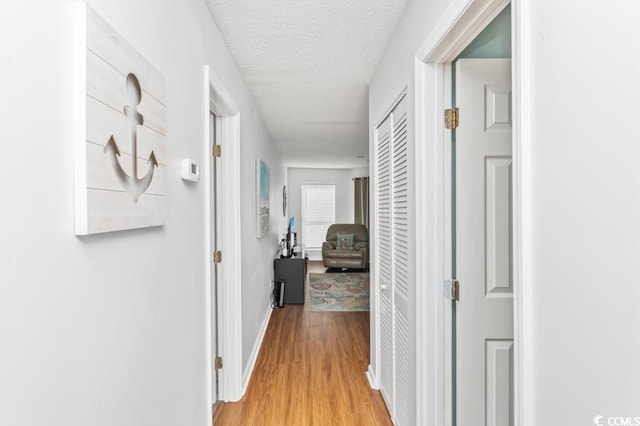 hallway with a textured ceiling and light hardwood / wood-style flooring