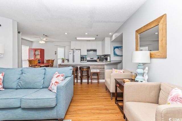 living room featuring light hardwood / wood-style flooring, a textured ceiling, and ceiling fan