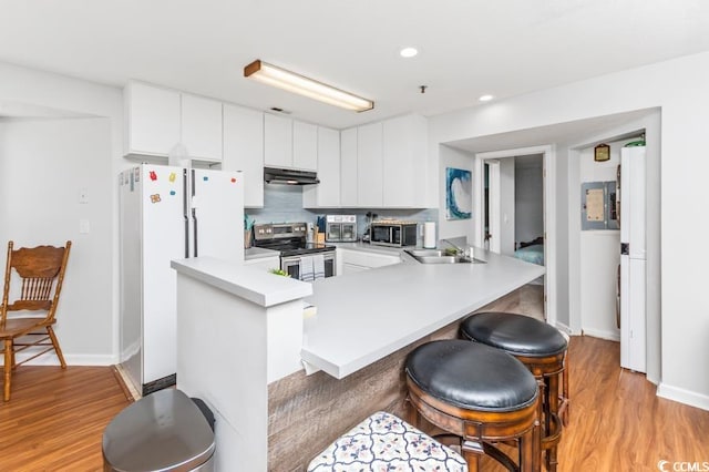 kitchen featuring kitchen peninsula, stainless steel appliances, a kitchen bar, light wood-type flooring, and white cabinets