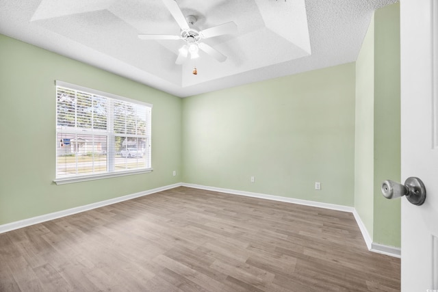 spare room with a textured ceiling, light hardwood / wood-style flooring, a tray ceiling, and ceiling fan