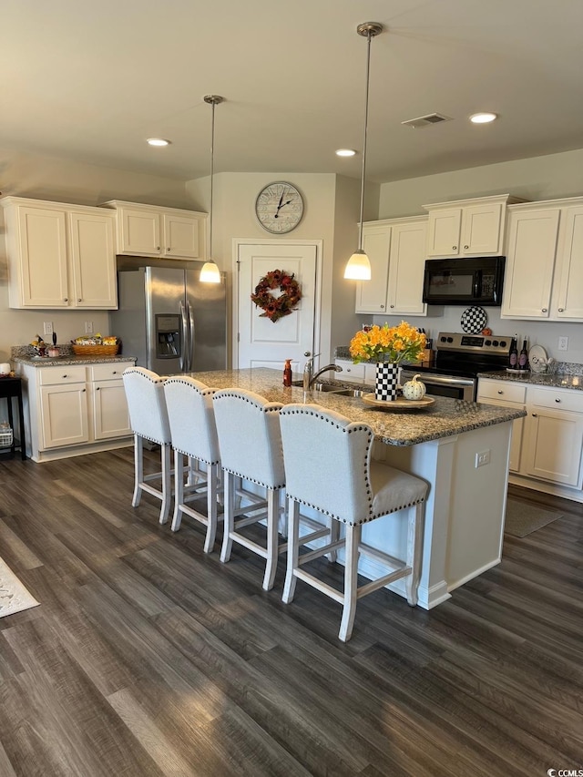 kitchen featuring appliances with stainless steel finishes, hanging light fixtures, white cabinetry, dark wood-type flooring, and a kitchen island with sink