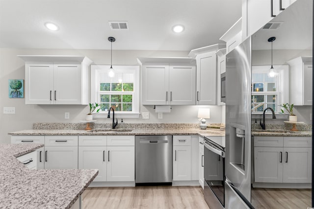 kitchen featuring white cabinets, sink, light wood-type flooring, appliances with stainless steel finishes, and decorative light fixtures