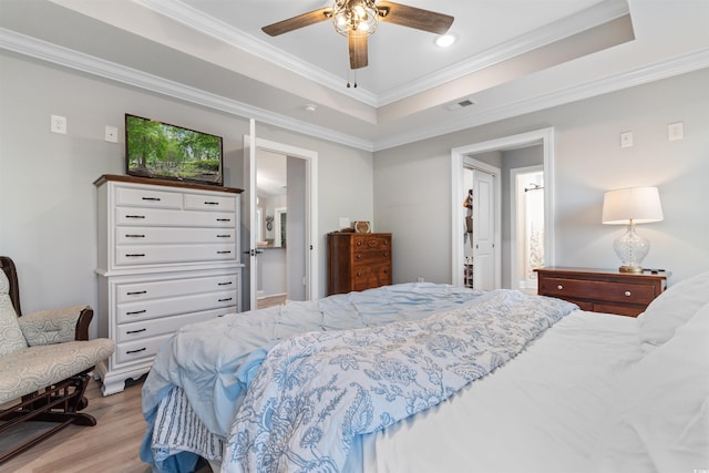 bedroom with a tray ceiling, ceiling fan, crown molding, and light hardwood / wood-style flooring