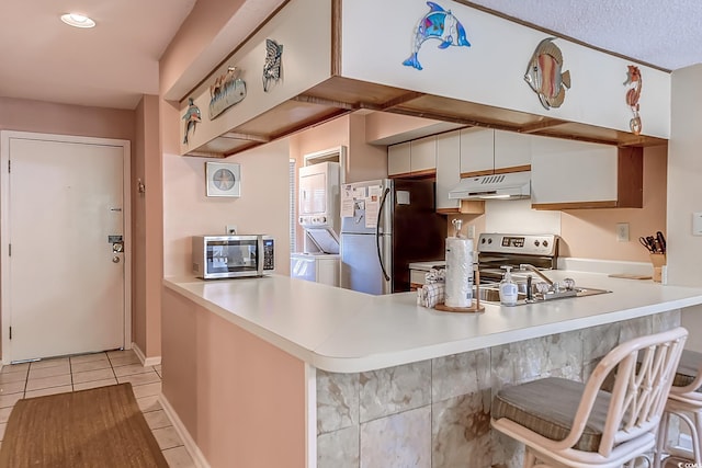 kitchen featuring kitchen peninsula, white cabinets, light tile patterned floors, stacked washer / drying machine, and stainless steel appliances