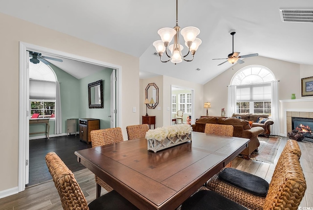 dining space with a tiled fireplace, vaulted ceiling, ceiling fan with notable chandelier, and hardwood / wood-style floors