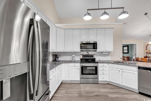 kitchen with sink, hanging light fixtures, dark stone countertops, appliances with stainless steel finishes, and white cabinets