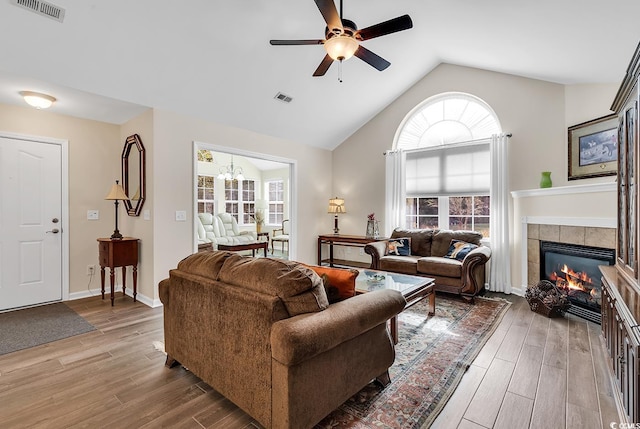 living room featuring lofted ceiling, wood-type flooring, a fireplace, and ceiling fan with notable chandelier