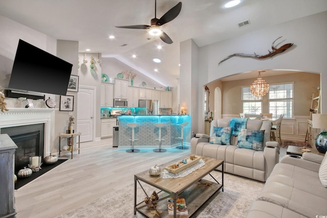 living room with ceiling fan with notable chandelier, high vaulted ceiling, and light hardwood / wood-style flooring