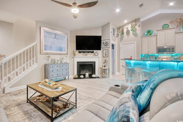 living room featuring ceiling fan, lofted ceiling, sink, and light hardwood / wood-style flooring