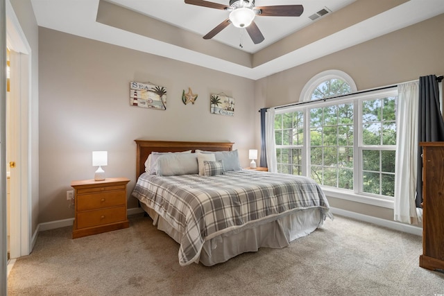 carpeted bedroom featuring a tray ceiling and ceiling fan