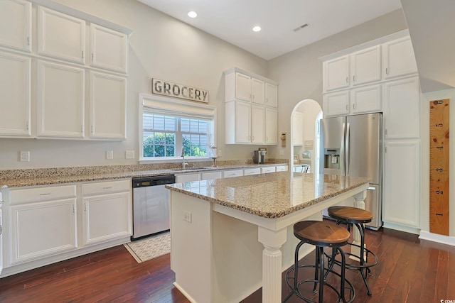 kitchen featuring stainless steel appliances, white cabinetry, light stone counters, a center island, and dark wood-type flooring