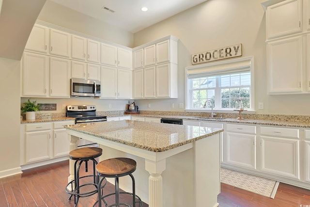 kitchen featuring stainless steel appliances, white cabinets, dark wood-type flooring, and a kitchen island