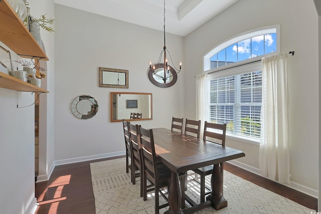 dining space with dark wood-type flooring, a healthy amount of sunlight, a raised ceiling, and a notable chandelier