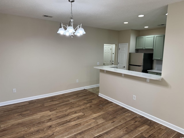 kitchen featuring green cabinets, dark hardwood / wood-style floors, stainless steel refrigerator, a chandelier, and pendant lighting