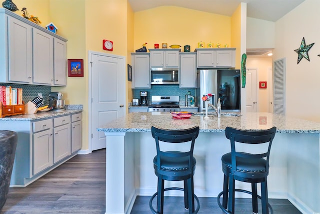 kitchen featuring a center island with sink, dark hardwood / wood-style flooring, appliances with stainless steel finishes, gray cabinets, and light stone counters