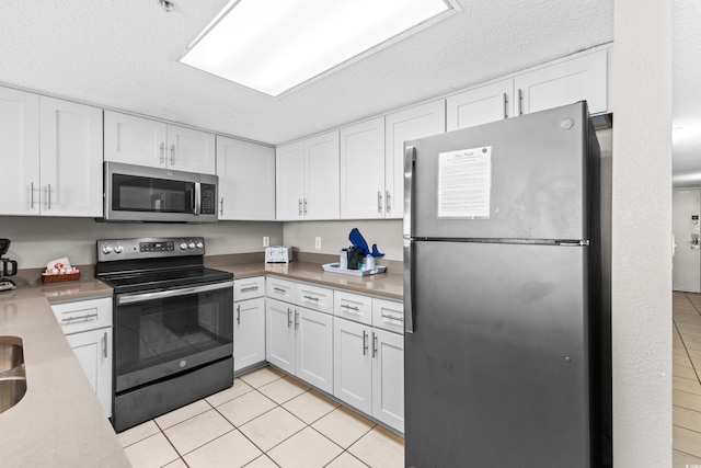 kitchen with a textured ceiling, white cabinets, stainless steel appliances, and light tile patterned floors