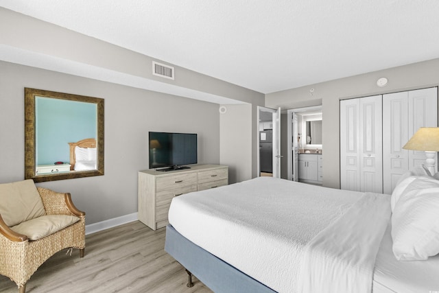 bedroom featuring light wood-type flooring, ensuite bath, and a closet