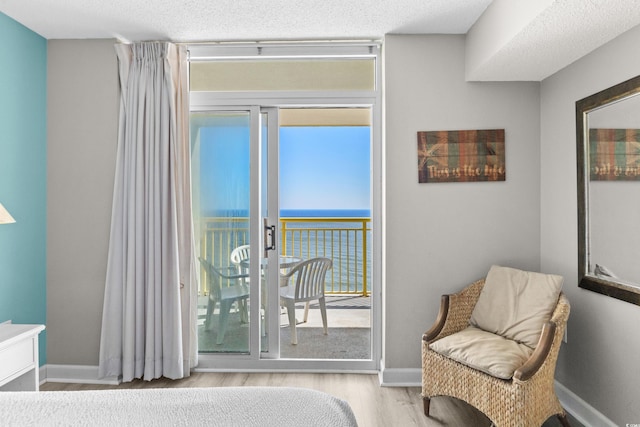 bedroom with access to exterior, a water view, a textured ceiling, and light wood-type flooring