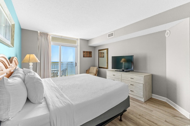 bedroom featuring access to exterior, light hardwood / wood-style floors, and a textured ceiling