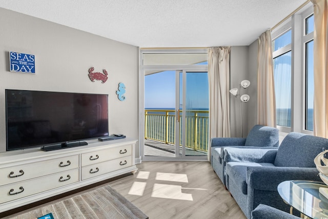 living room featuring floor to ceiling windows, a water view, a textured ceiling, and light hardwood / wood-style flooring