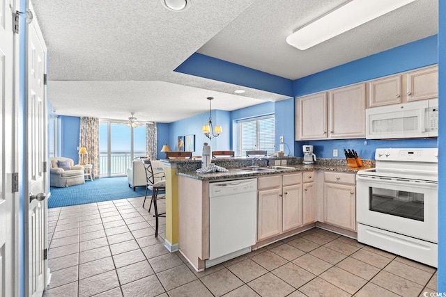 kitchen featuring a peninsula, white appliances, open floor plan, a textured ceiling, and a sink