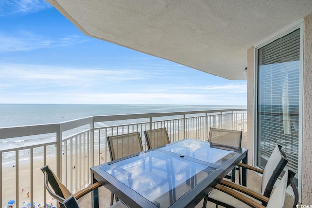balcony with a water view, outdoor dining area, and a view of the beach