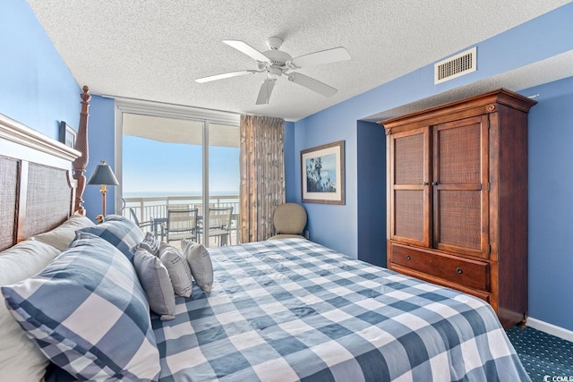 carpeted bedroom with ceiling fan, access to outside, a textured ceiling, floor to ceiling windows, and a water view