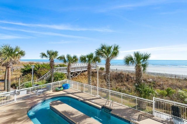 view of pool with a fenced in pool, a water view, fence, and a beach view
