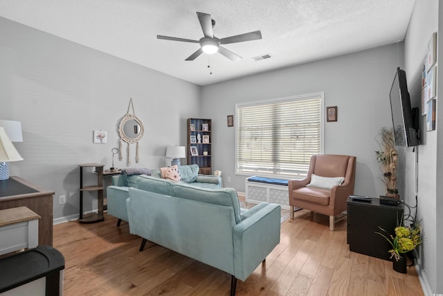 living room with ceiling fan, a textured ceiling, and light hardwood / wood-style flooring