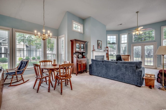 dining space featuring a high ceiling, light colored carpet, ceiling fan with notable chandelier, and plenty of natural light