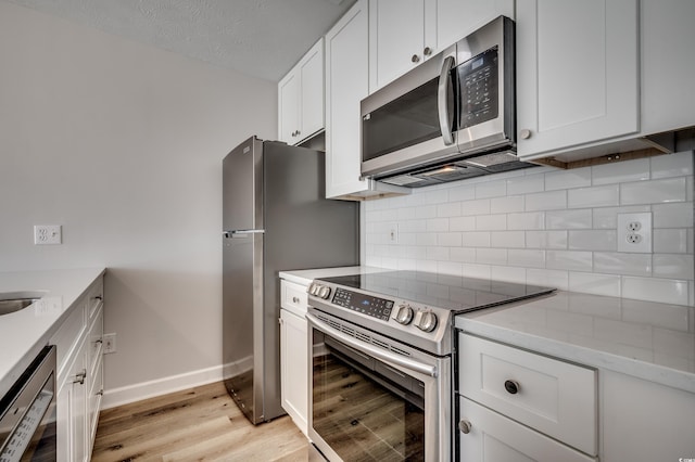 kitchen with white cabinets, backsplash, appliances with stainless steel finishes, light stone countertops, and light hardwood / wood-style flooring