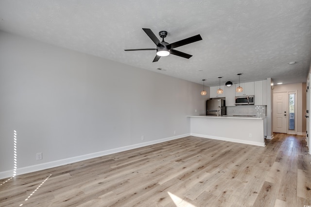 unfurnished living room featuring light hardwood / wood-style flooring, a textured ceiling, and ceiling fan