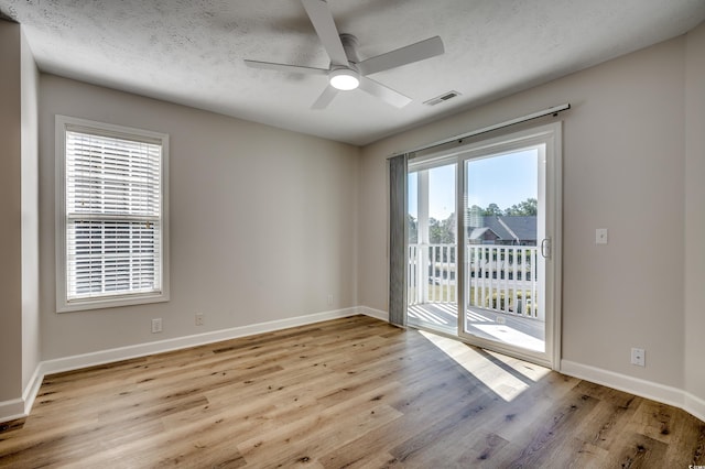 unfurnished room featuring a textured ceiling, a healthy amount of sunlight, light wood-type flooring, and ceiling fan