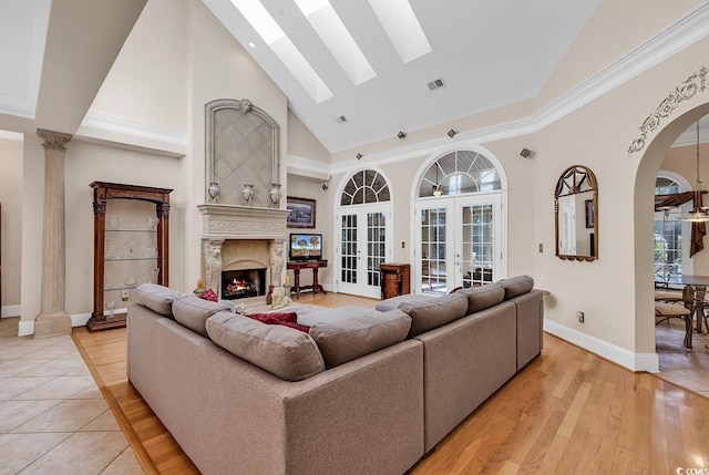 living room with a fireplace, a skylight, high vaulted ceiling, light wood-type flooring, and french doors