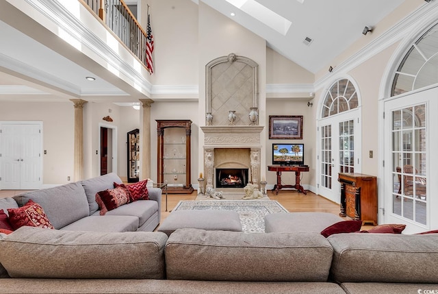 living room featuring a towering ceiling, a high end fireplace, decorative columns, and light wood-type flooring